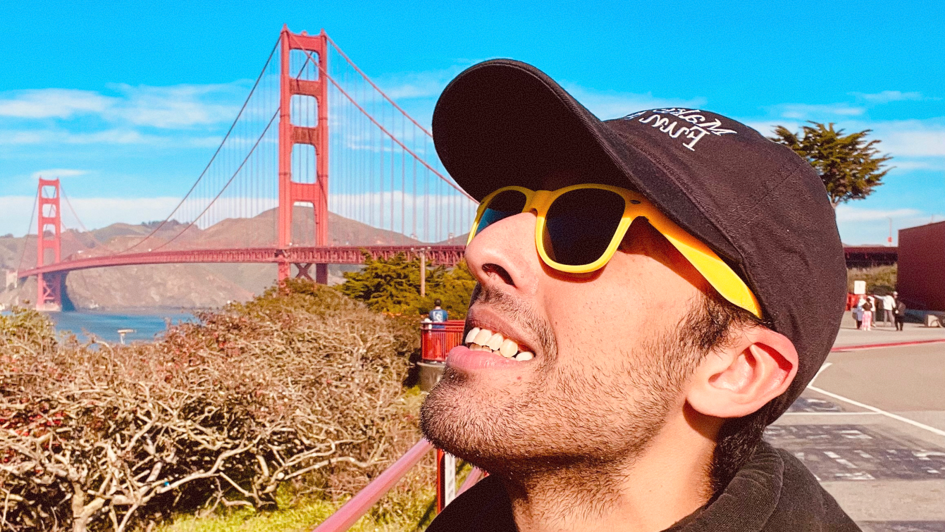 Adil Mania in a cap and yellow sunglasses, the Golden Gate Bridge behind him