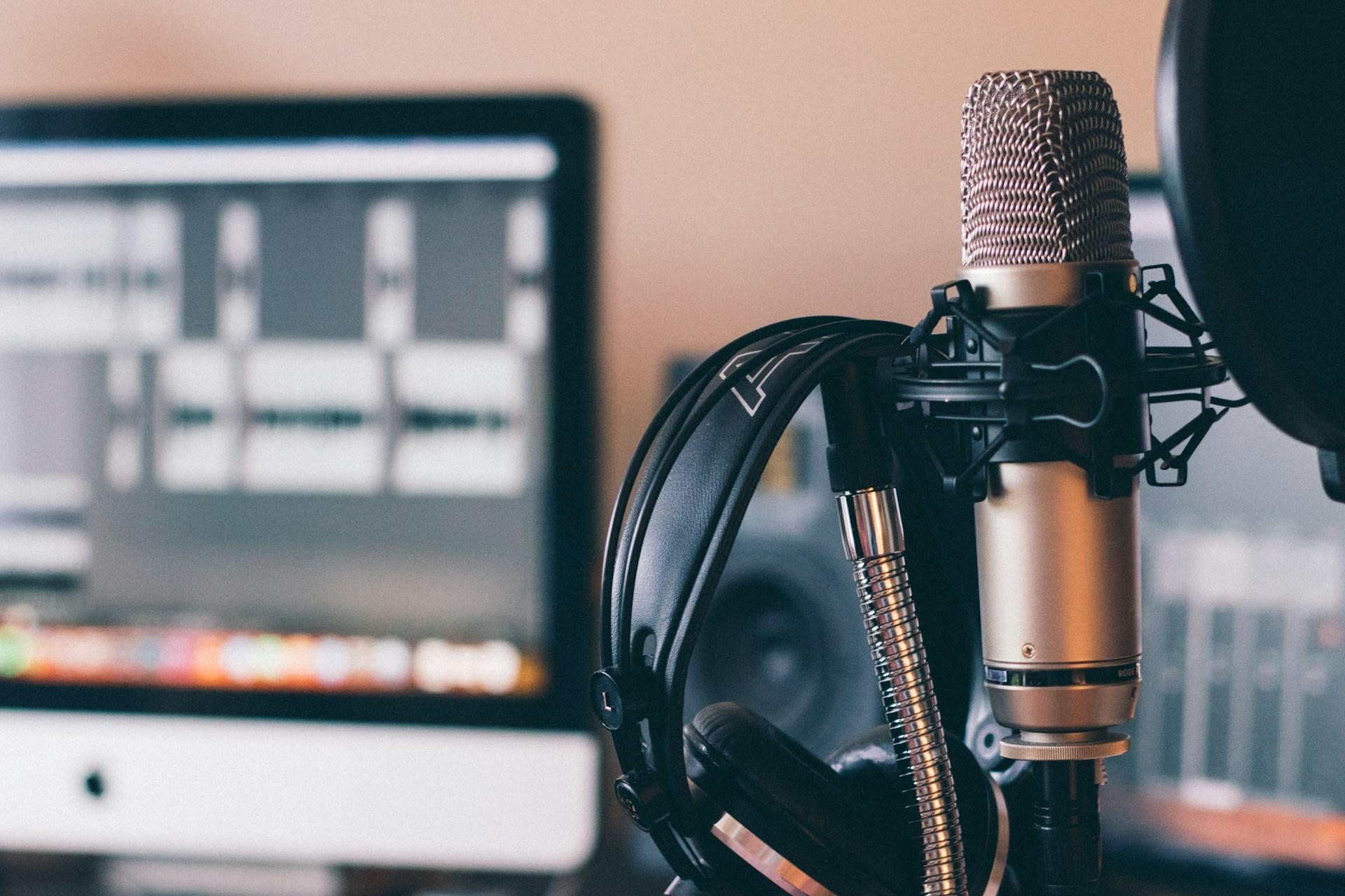 A studio microphone and headphones in front of an editing monitor