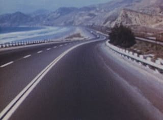 A curving coast road between the sea and hills