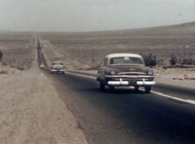 A 1950s car on a straight desert highway
