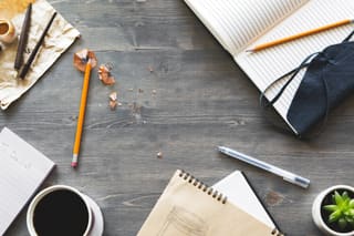 A desk from above with notebooks, pencils and coffee