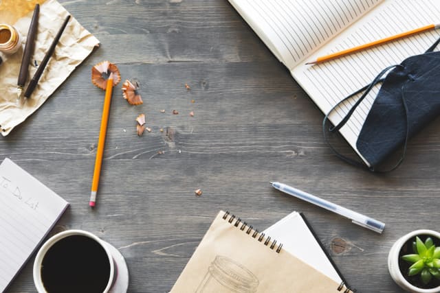 A desk from above with notebooks, pencils and coffee