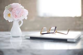 Pink flowers in a white jug beside glasses on marble
