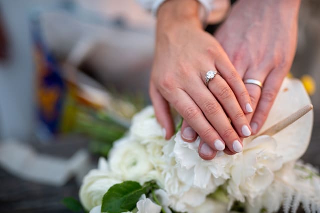 Hands wearing wedding rings resting on white roses