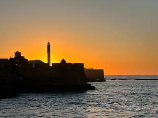 A lighthouse and harbour wall in silhouette at sunset