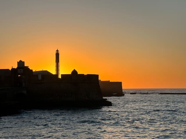 A lighthouse and harbour wall in silhouette at sunset