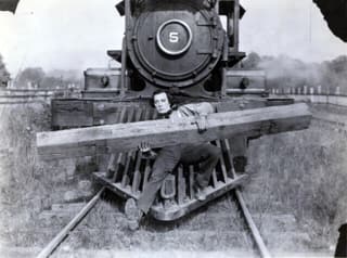 A man holding a railway sleeper on the cow-catcher of a steam locomotive, from The General