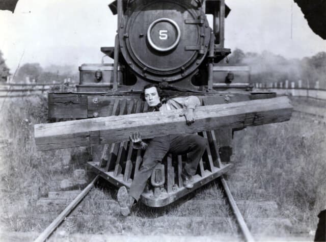 A man holding a railway sleeper on the cow-catcher of a steam locomotive, from The General