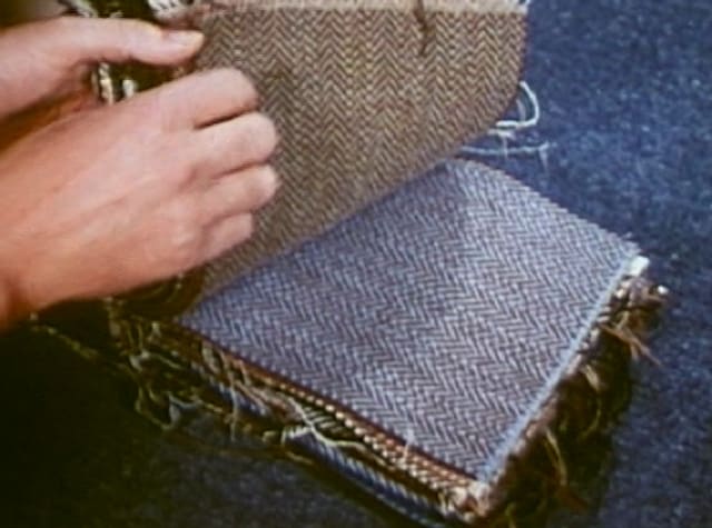 A hand turning over tweed fabric samples